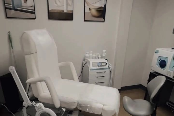 Gabinet podologiczny: biały fotel zabiegowy, lampa z lupą i sprzęt przy ścianie